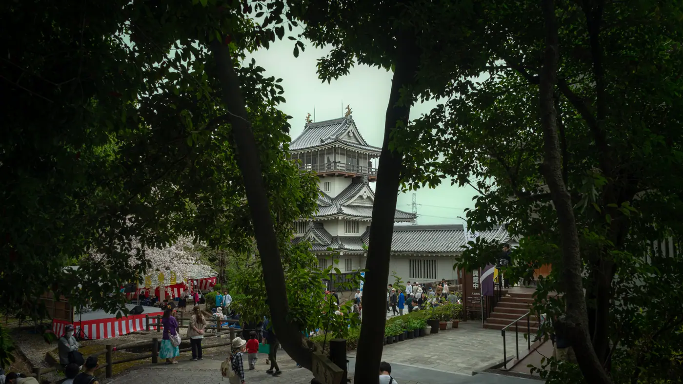 Festival stalls and visitors below Iwasaki Castle during cherry blossom season