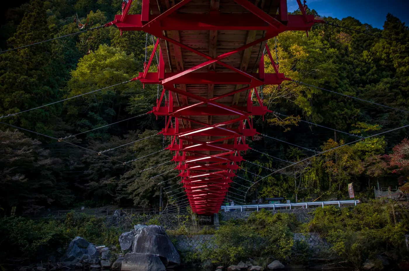 Looking up at the underside of the red bridge between green trees