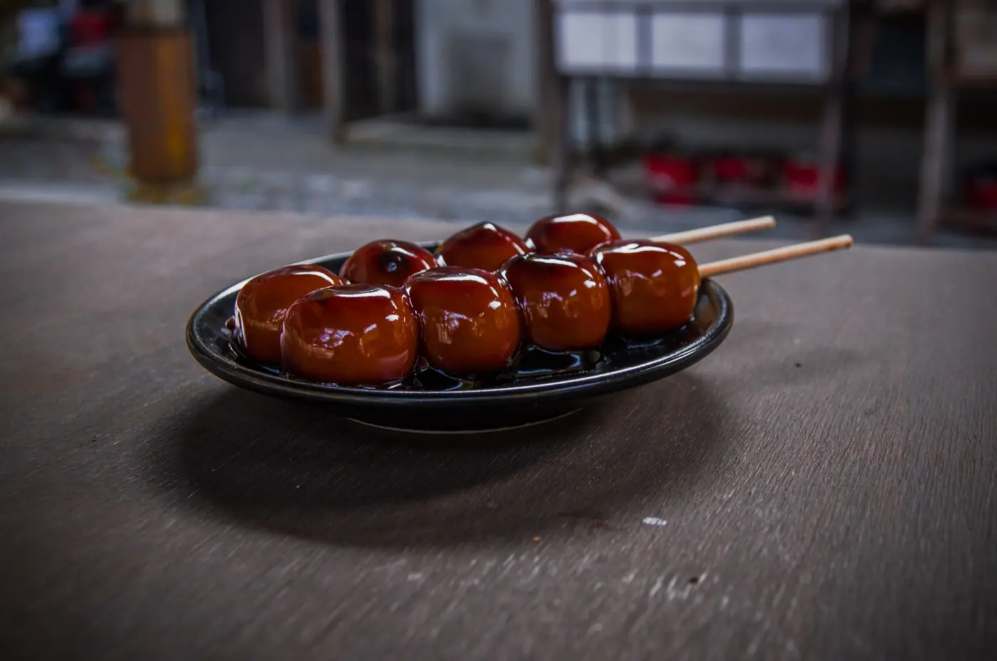 Five glazed dango on a skewer, served on a black plate