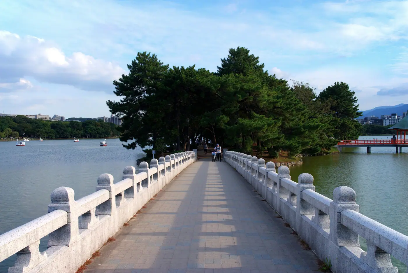 A white stone bridge leading to a pine-covered island in Ohori Park
